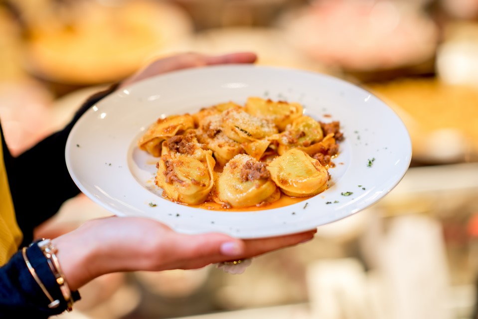Bolonia Włochy.Holding a plate with traditional ring-shaped pasta tortellini with bolognese in front of the food showcase background in Bologna city