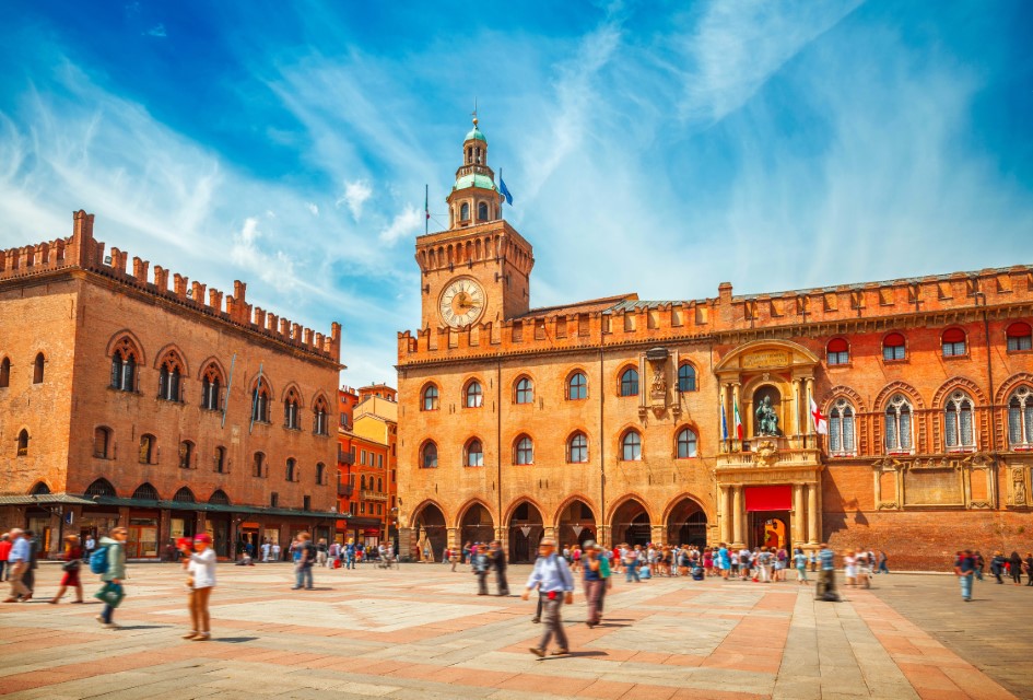 Bolonia Włochy. Piazza Maggiore w Bolonii starej wieży ratusza z dużym zegarem i błękitnym niebem na tle. Antyczne budynki galerie z terakoty