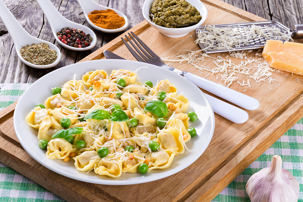 Delicious tortellini with green peas, fried Pine nuts, decorated with basil leaves on a white dish with spice, sauce pesto and parmesan cheese on an old rustic table, italian style. close-up