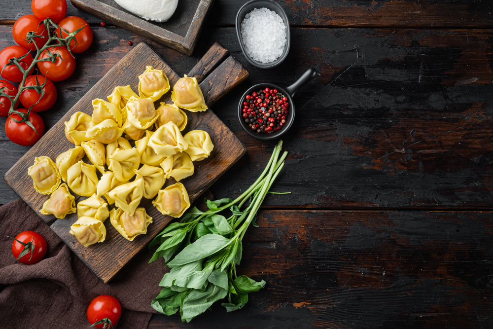 Homemade Tortellini with cheese and basil set, on wooden cutting board, on old dark wooden table background, top view flat lay, with copy space for text