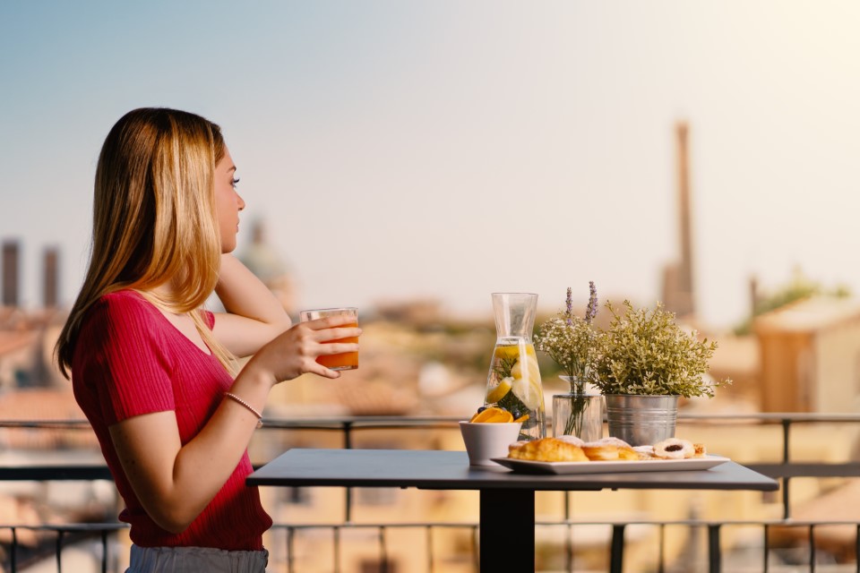 Noclegi w Bolonii, Young woman portrait having breakfast outdoors in hotel terrace looking at panorama of the city. Twin Towers in the background.