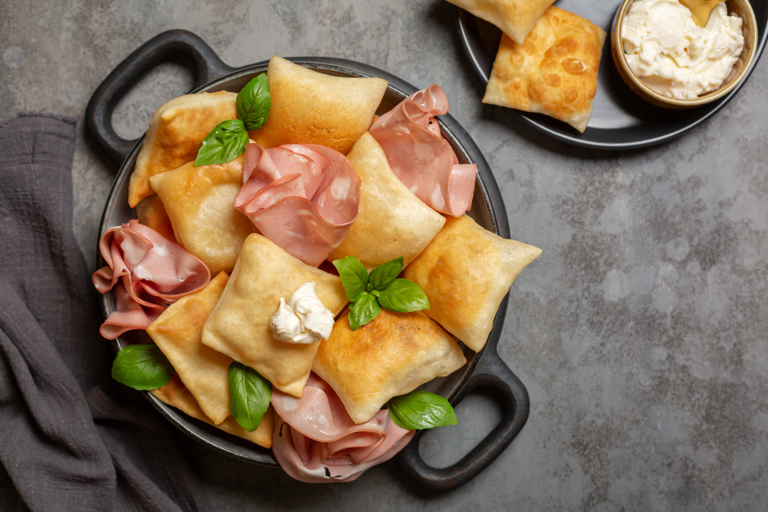 Emilia Romania, Top view of Italian appetizer. Fried bread crescentine or gnocco fritto with mortadella and soft cheese, decorated with basil leaves. Traditional food.