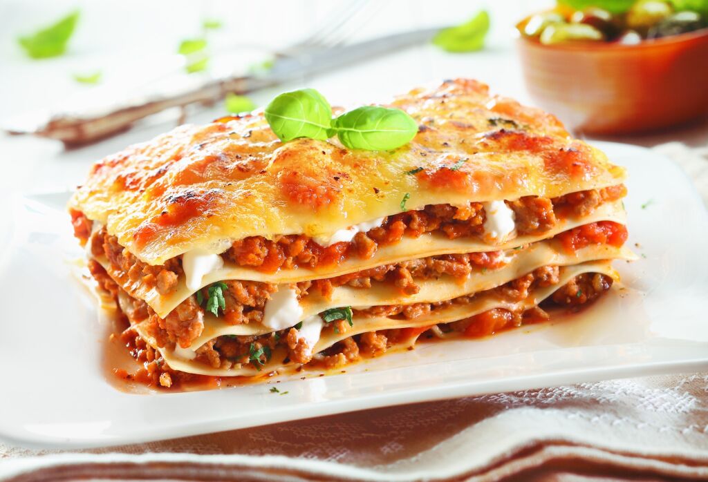 Zbliżenie tradycyjnej lasagne z mielonego sosu bolognese wołowiny z liśćmi bazylii podawane na białym talerzu