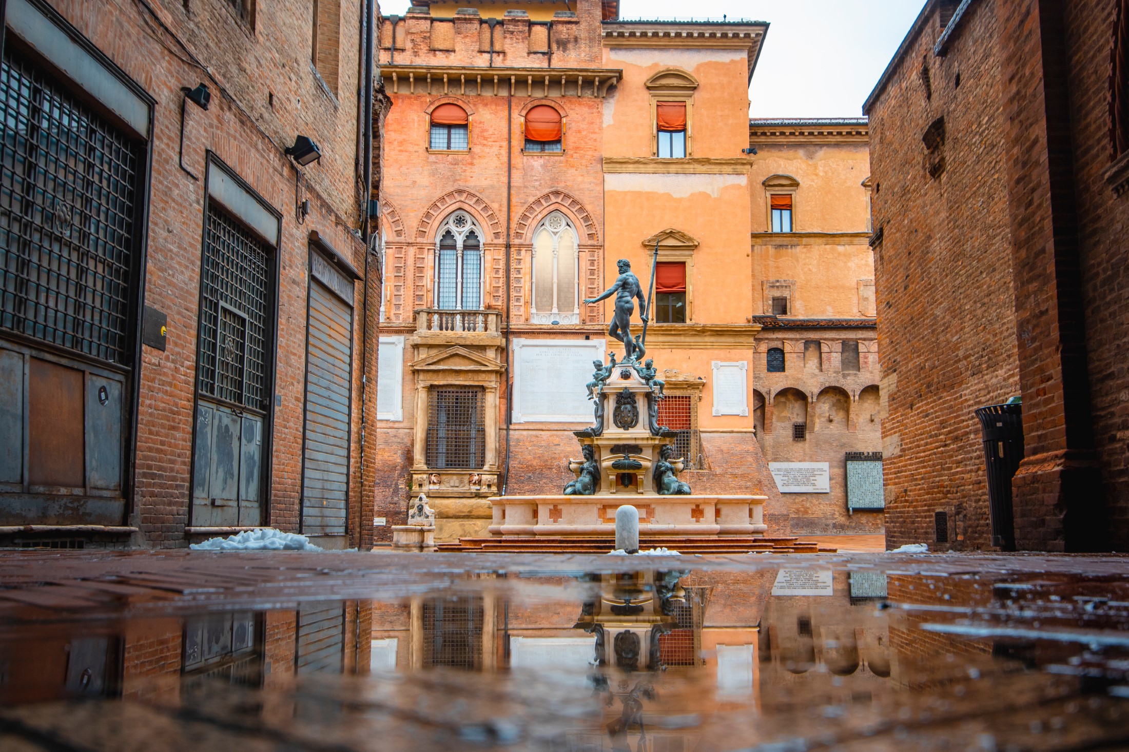Zwiedzanie Bolonii podczas brzydkiej pogody: Atrakcje na każdą pogodę!Bologna in the morning, looking Neptune statue in main square with sunlight and reflection in a puddle on the street